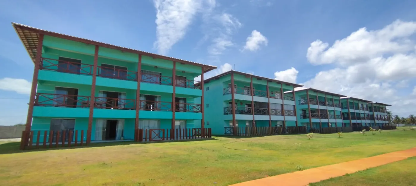 Blocos turquesa de três andares do Villa das Águas, com varandas de madeira e gramado extenso